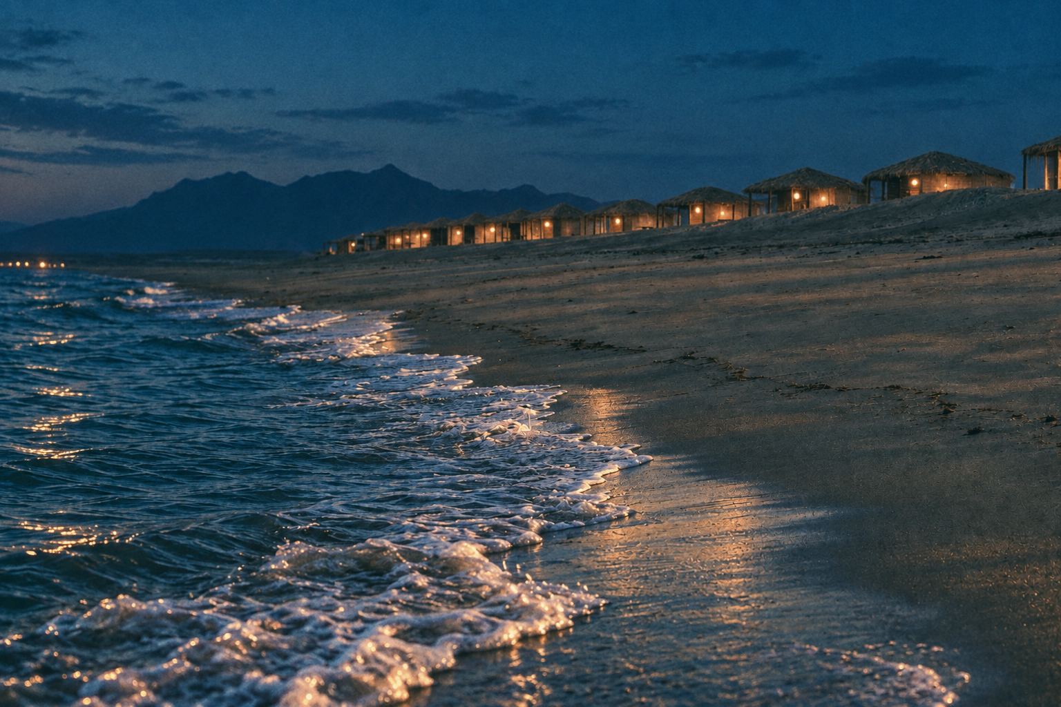 A long Sinai beach at blue hour, thatched huts lit from inside along the dune and surf foam running up the wet sand.