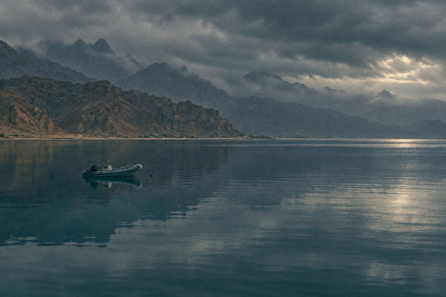 A small rescue boat, tiny on dark still Gulf water under a heavy storm sky, with mountains half lost in cloud.