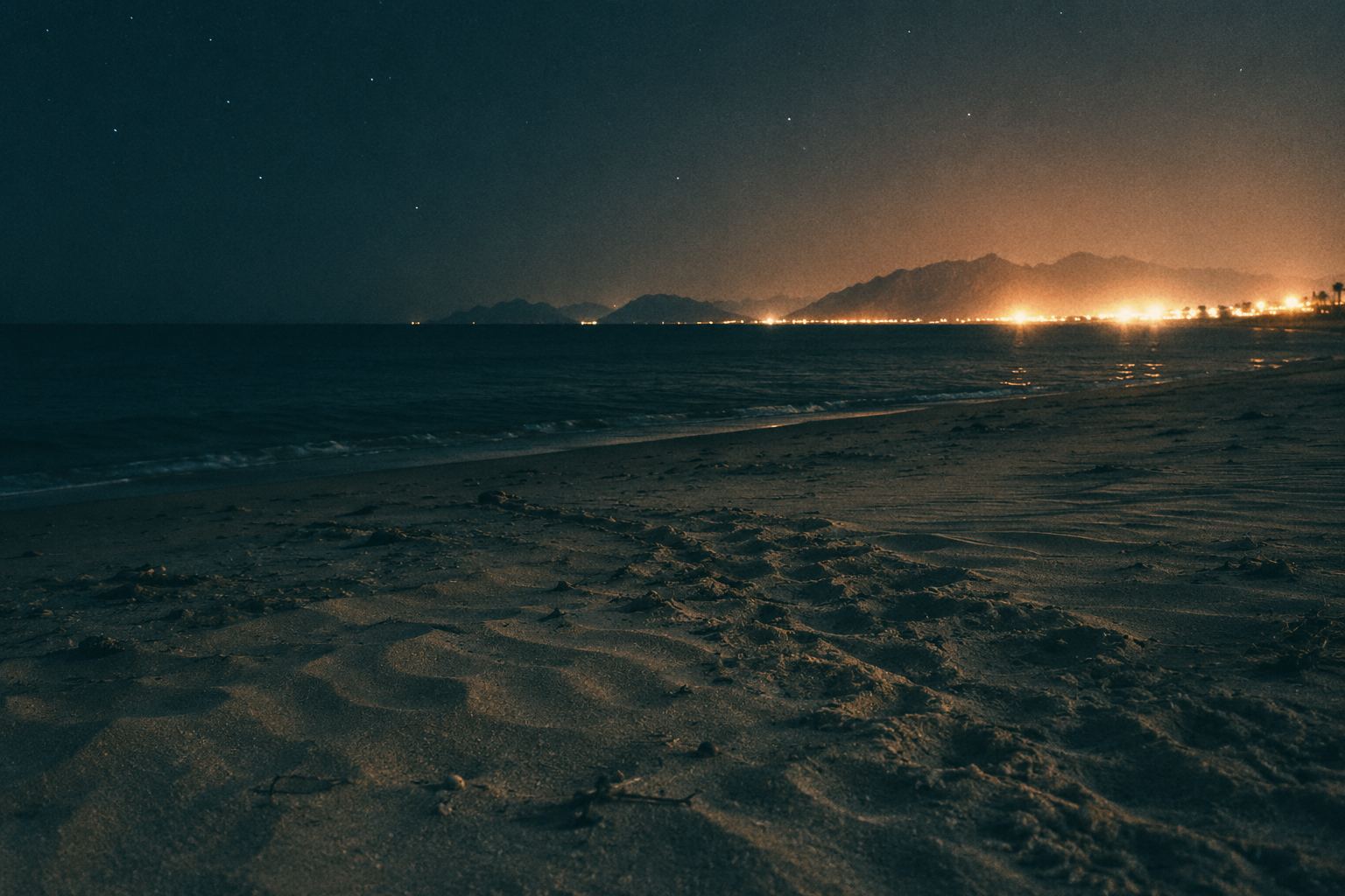 A dark nesting beach at night with harsh resort lights glowing on the horizon.